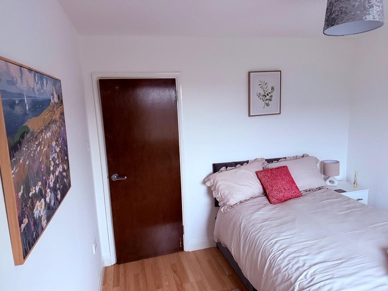 Bedroom with double bed, pink and red pillows, wooden floor, dark door and wall art
