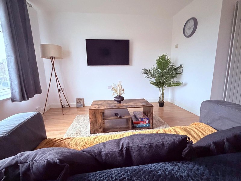 Modern living room with black sofa, wooden TV unit, potted plant and floor lamp