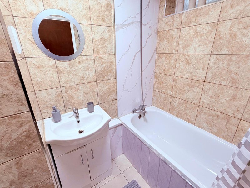 Bathroom with beige tiles, white sink vanity, bathtub, and circular mirror