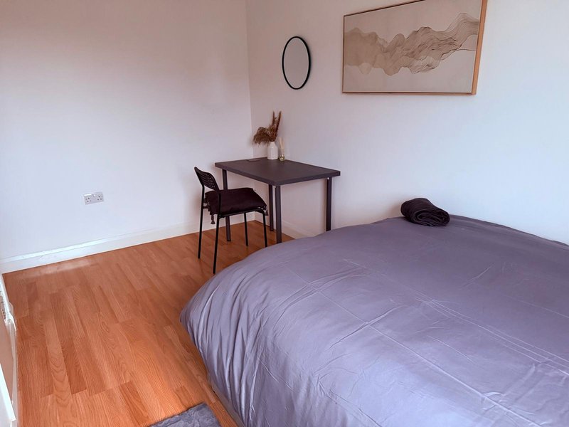 Bedroom with purple duvet, wooden desk, chair, and laminate flooring