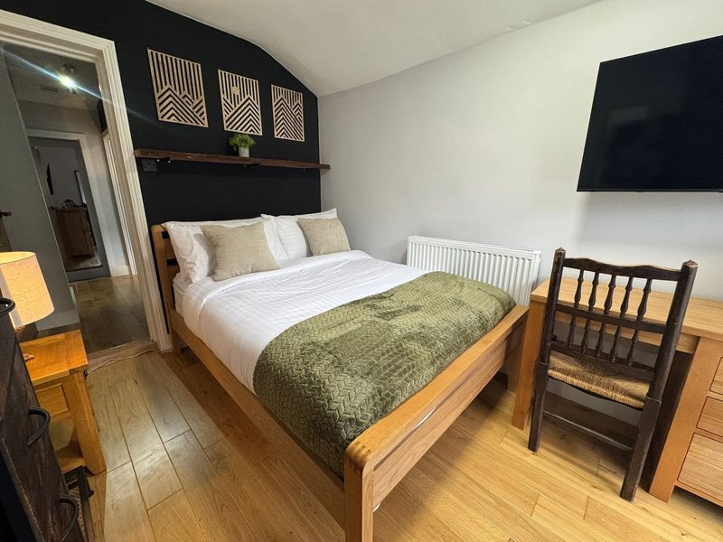 Bedroom with wooden bed, green throw blanket, wall-mounted TV and geometric wall art