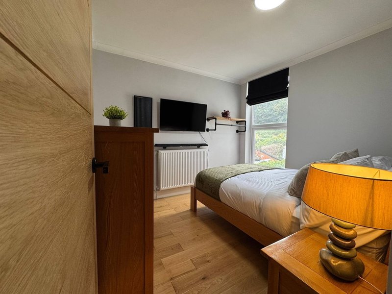 Bright bedroom with single bed, wooden furniture, desk with monitor, and window with black blind
