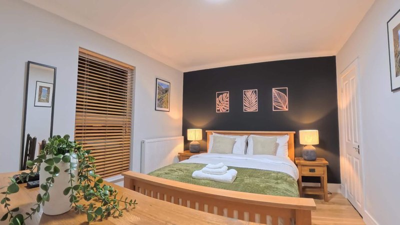 Modern bedroom with double bed, wooden frame, black accent wall, bedside lamps and potted plant