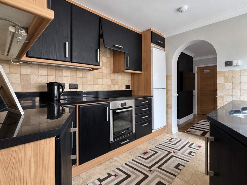 Modern kitchen with black cabinetry, wooden accents, beige tile backsplash, and geometric floor runner