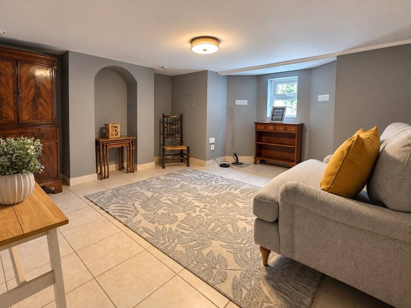 Spacious basement living room with beige sofa, wooden furniture, area rug and recessed lighting