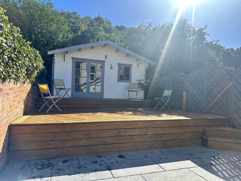 Garden studio cabin with decking, two chairs, and brick boundary wall