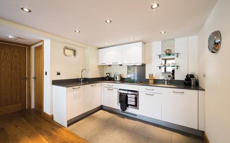 Modern kitchen with white cabinetry, black countertops, stainless steel appliances and wooden flooring