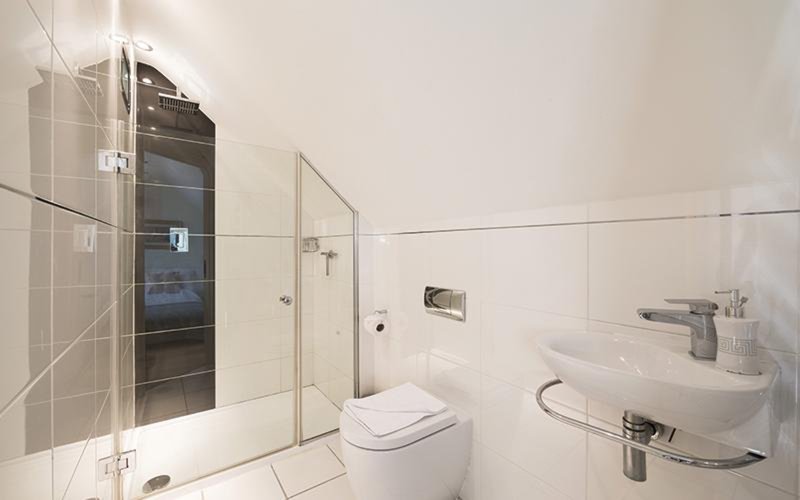 Modern bathroom with walk-in shower, toilet, sink and white tile walls