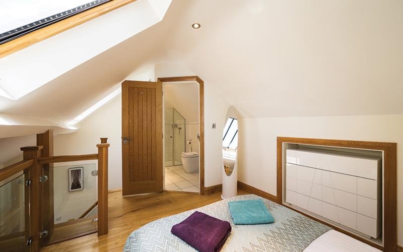 Bright attic bedroom with wooden flooring, double bed, and ensuite bathroom visible through open door