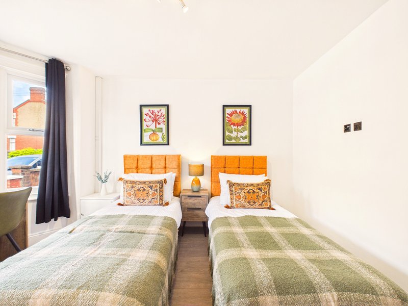 Twin bedroom with two single beds, orange headboards, floral wall art and window with dark curtains
