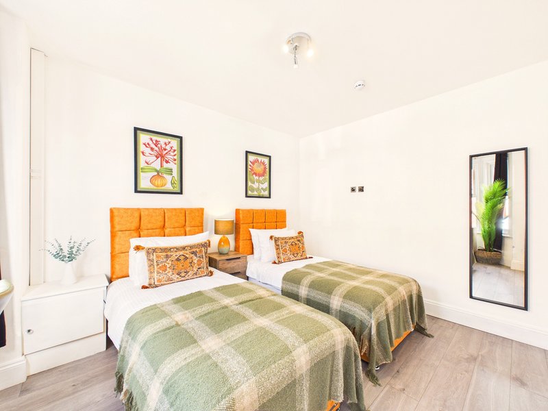 Twin bedroom with orange headboards, checkered bedspreads, framed botanical artwork, and wooden flooring