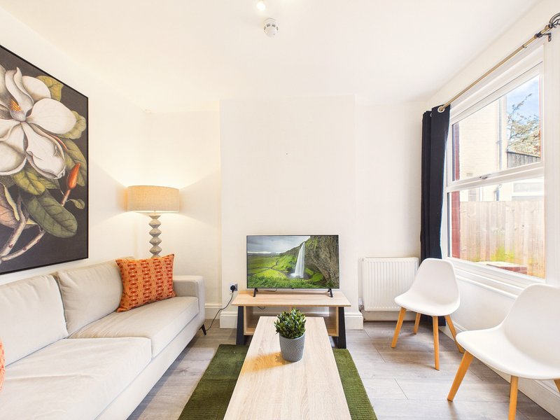 Bright living room with cream sofa, white chairs, TV on stand, and wall art