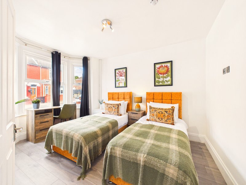 Bright twin bedroom with orange headboards, plaid blankets, wooden dresser and window