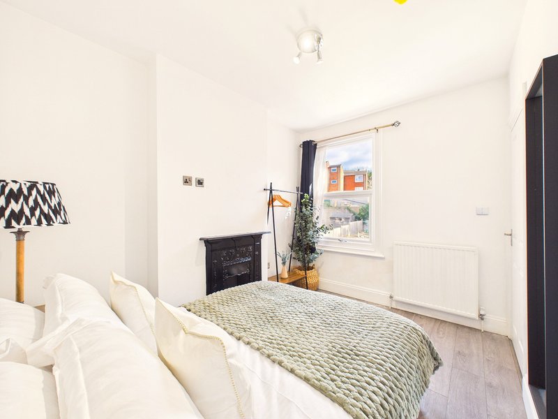 Bright bedroom with double bed, fireplace, window with curtains and wooden floor