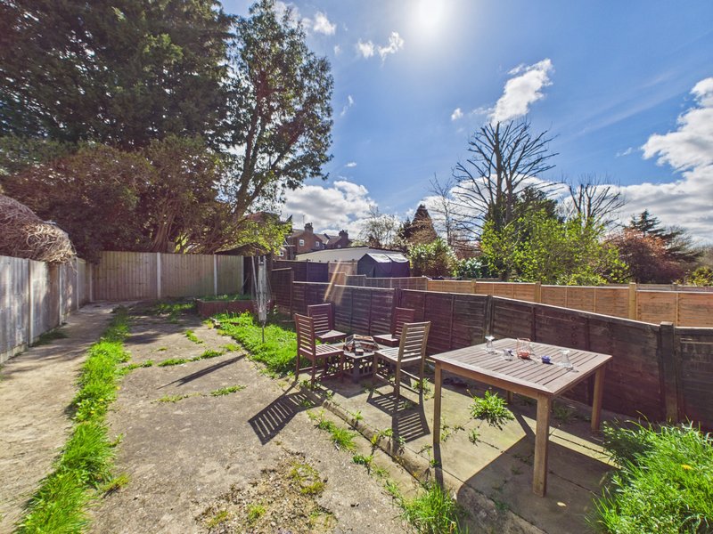 Rear garden with patio, wooden table, chairs, fencing and mature trees overhead