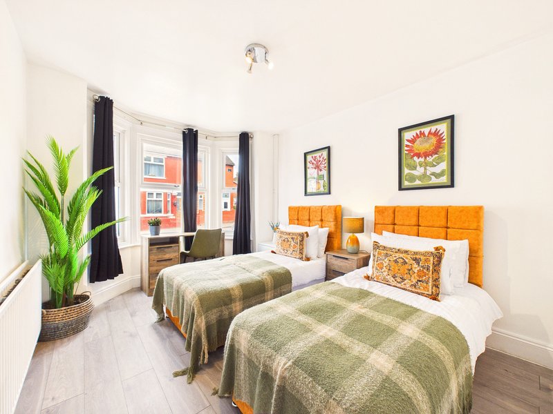 Twin bedroom with orange headboards, plaid bedding, potted plant, and street-view window