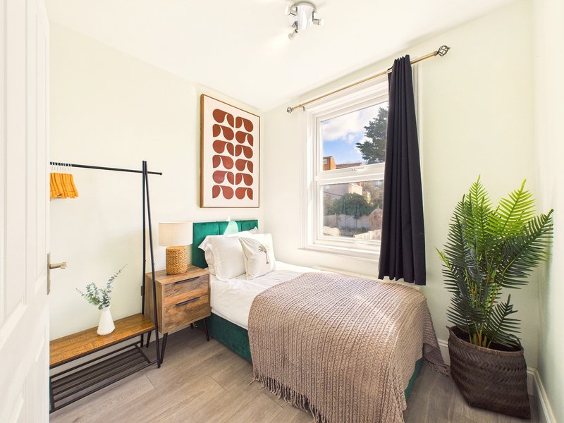 Bright bedroom with single bed, wooden nightstand, potted plant and window with countryside view