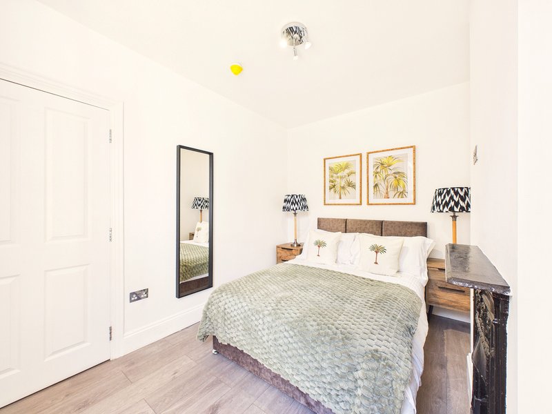 Bright bedroom with double bed, wooden floor, mirror, framed botanical prints and bedside table