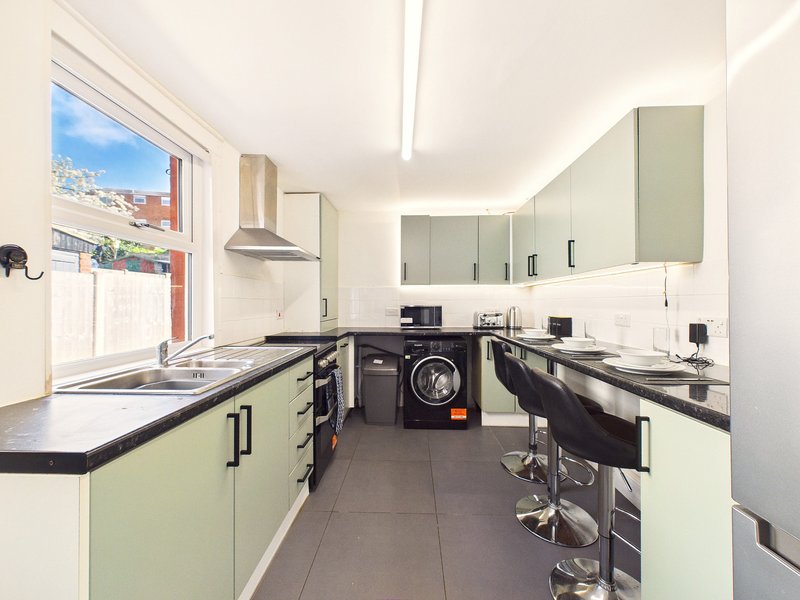 Modern galley kitchen with cream cabinetry, black countertops, washing machine and bright window