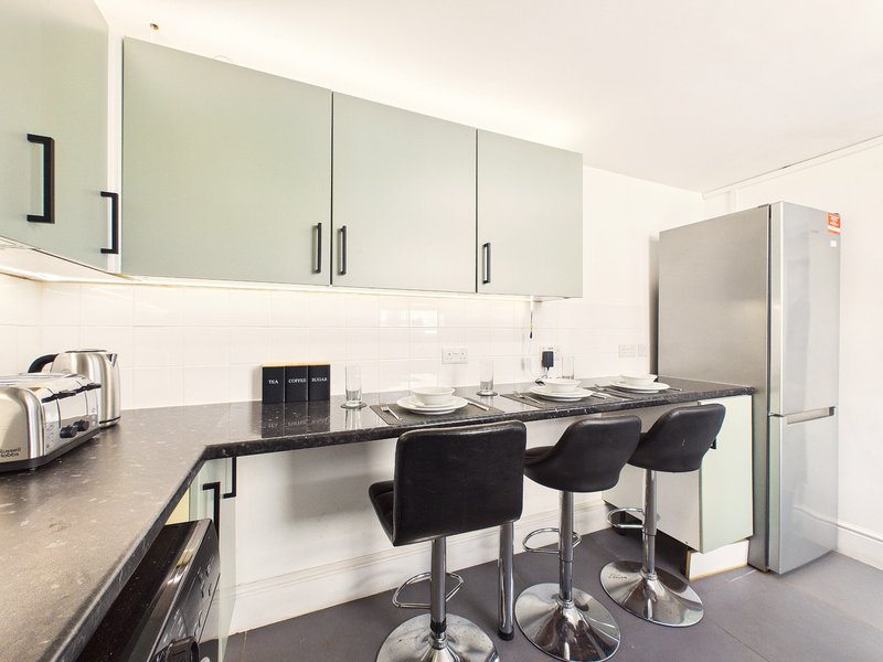 Modern kitchen with black countertop, green-fronted cabinets, stainless steel fridge, and breakfast bar seating