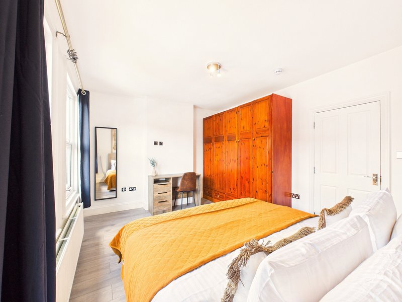 Spacious bedroom with double bed, orange wardrobe, wooden desk, and mirror