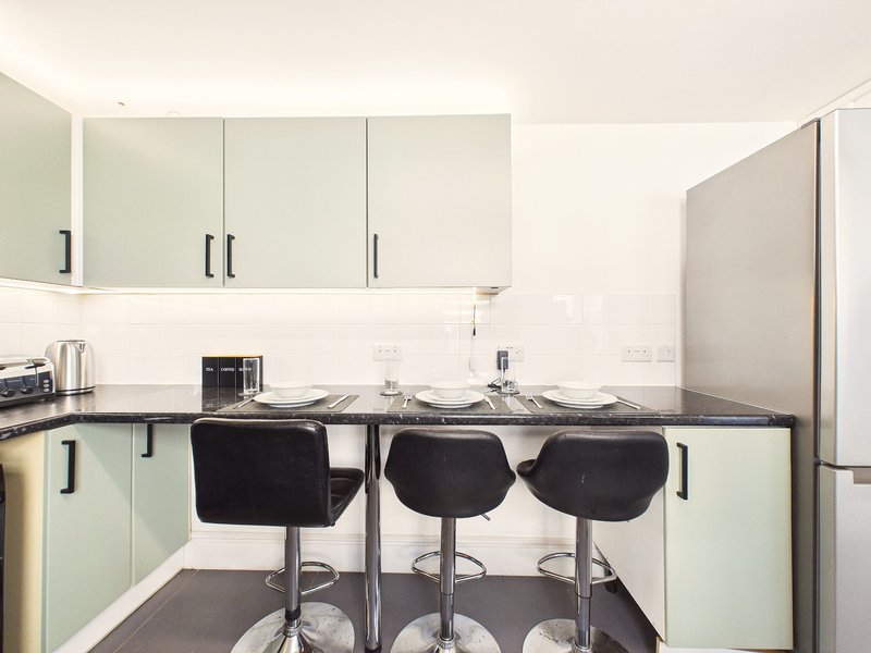 Modern kitchen with pale green cabinetry, black bar stools, and white subway tile backsplash