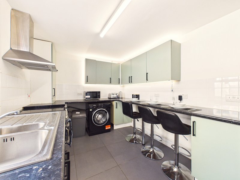 Modern kitchen with sage green cabinets, black appliances, white tile backsplash and breakfast bar seating
