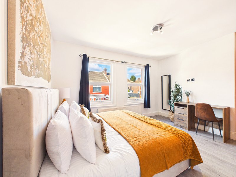 Bright bedroom with double bed, orange throw, white pillows, desk, mirror and garden views