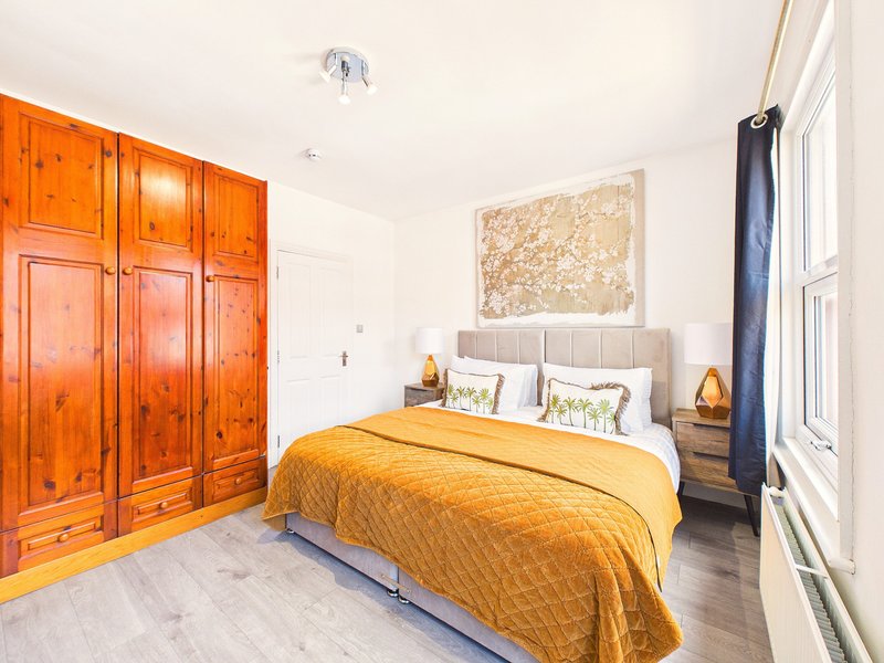 Bright bedroom with double bed, yellow bedding, wooden wardrobe, and artwork on wall