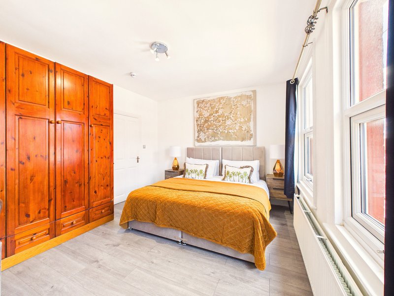 Bright bedroom with double bed, yellow bedding, wooden wardrobe and large windows