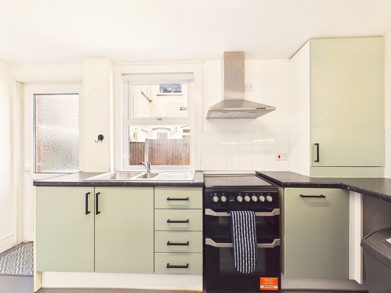 Modern kitchen with pale green cabinets, black countertop, stainless steel cooker hood and black electric range