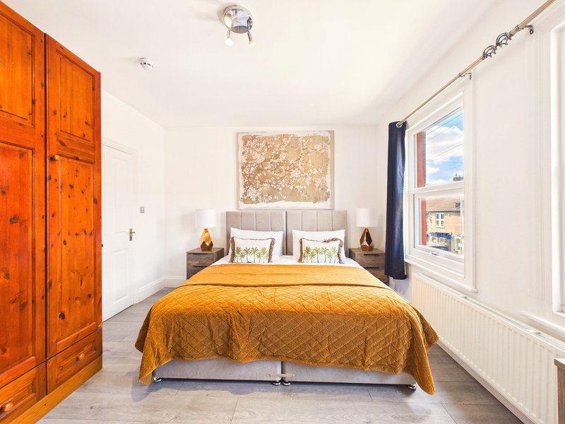 Bright bedroom with double bed, yellow bedding, wooden wardrobe and large window