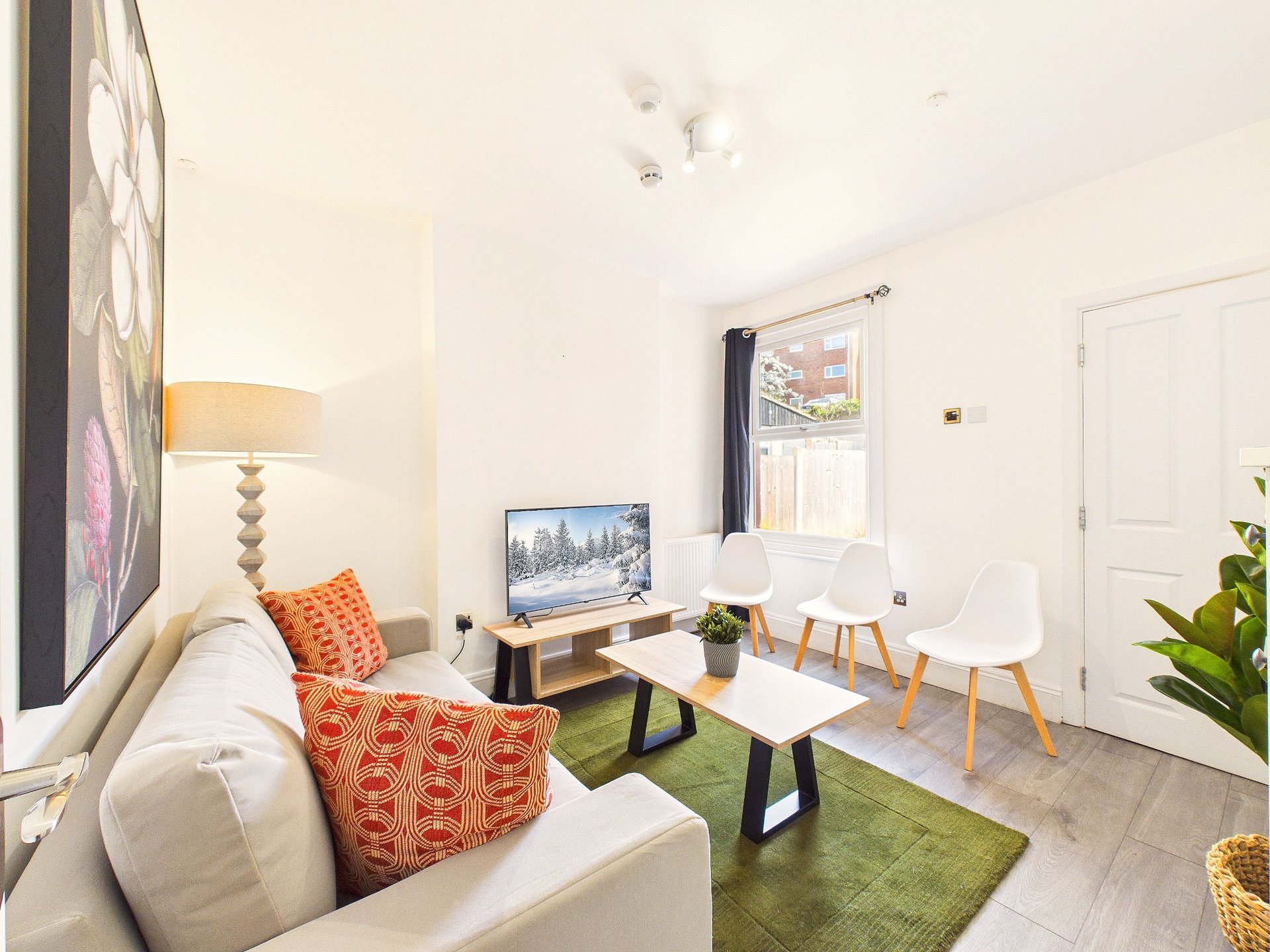 Modern living room with cream sofa, orange cushions, TV, desk, and green rug