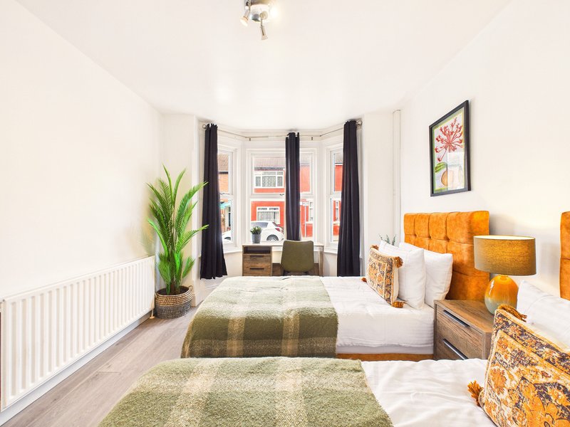 Bright bedroom with two single beds, large window, green plant, and orange headboards