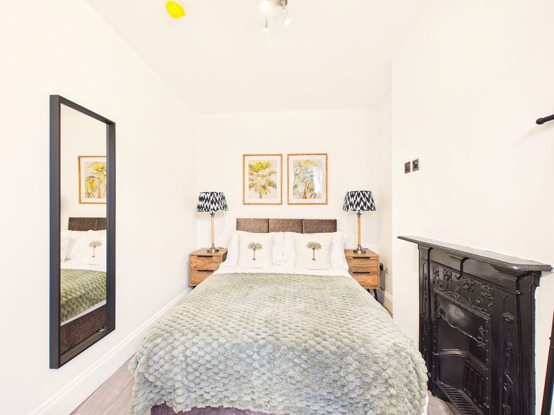 Bedroom with double bed, wooden bedside tables, framed botanical prints, and fireplace