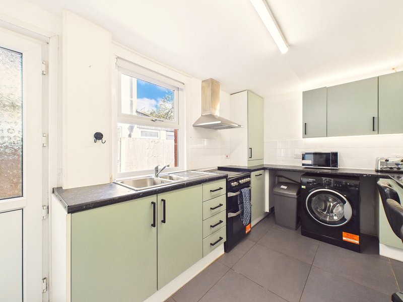 Modern kitchen with green cabinetry, black countertop, stainless steel appliances and washing machine