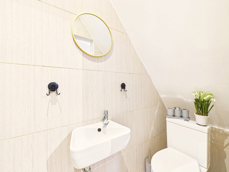 Compact bathroom with wall-mounted sink, round mirror, toilet, and potted plant