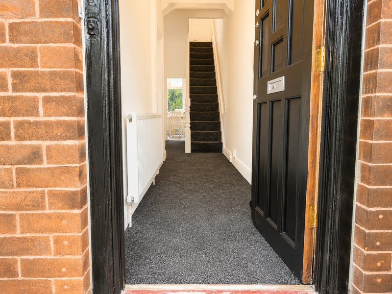 Narrow hallway with dark carpet, black doors, white walls, and stairs visible in distance