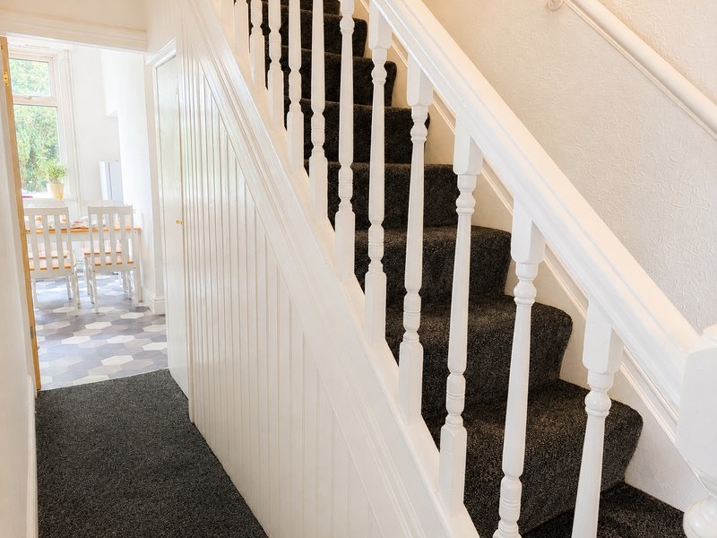 Staircase with dark carpeted steps, white railings, and bright hallway beyond