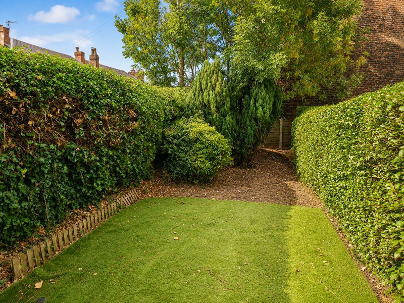 Garden pathway with manicured hedges, green lawn, brick walls and mature trees