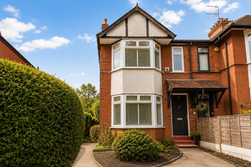 Red brick Edwardian house with bay windows, black door, and manicured front garden