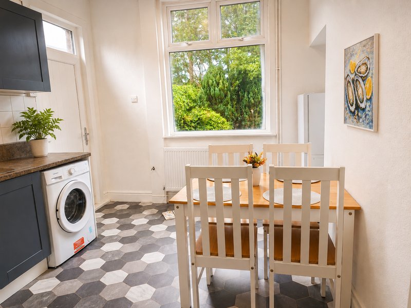 Kitchen and dining area with washing machine, wooden chairs, and large window overlooking garden