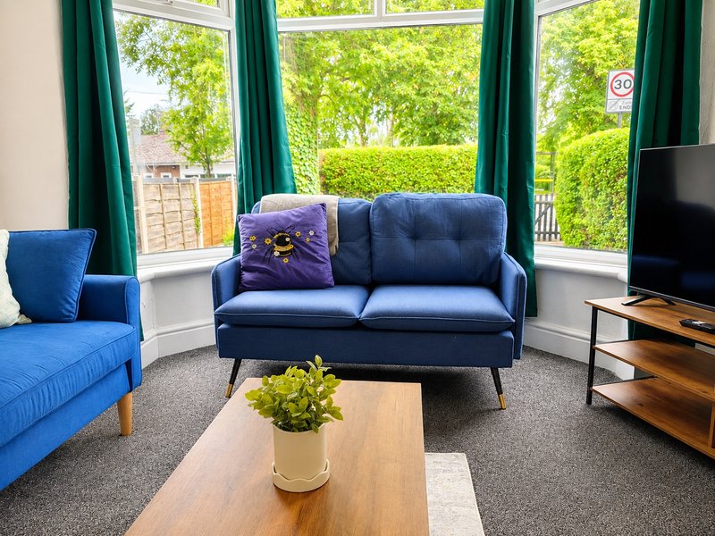 Bright living room with blue sofas, wooden coffee table, green curtains and garden views
