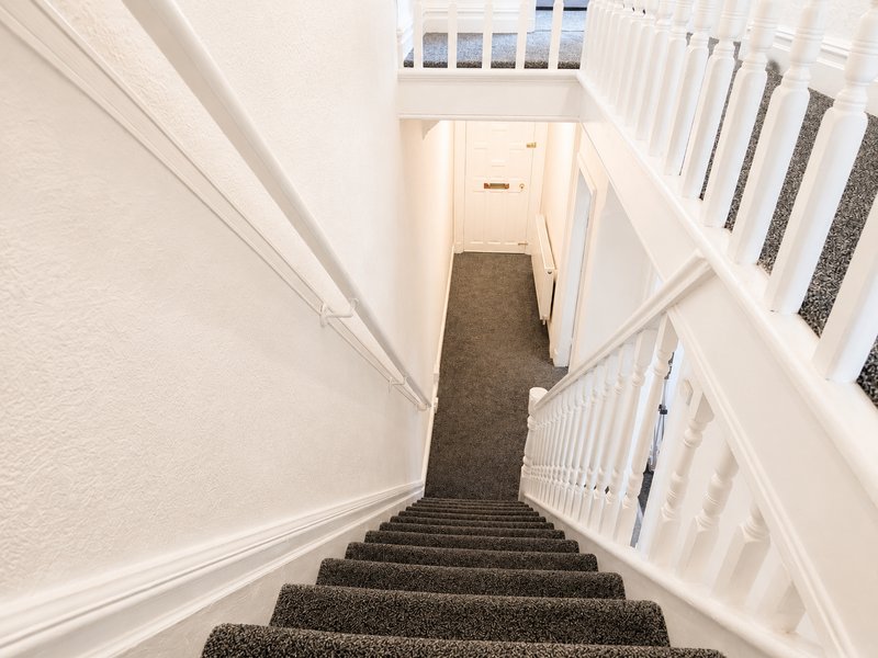Staircase with dark grey carpet, white walls and railings, view down to hallway