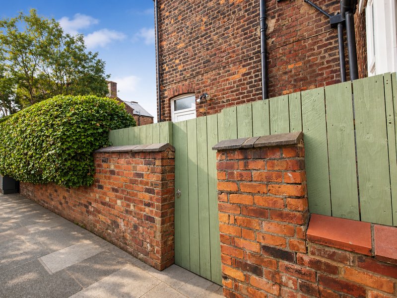 Brick exterior with green fence, hedging and paved driveway area