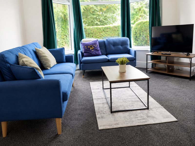 Bright living room with blue sofas, coffee table, TV, and large windows overlooking garden