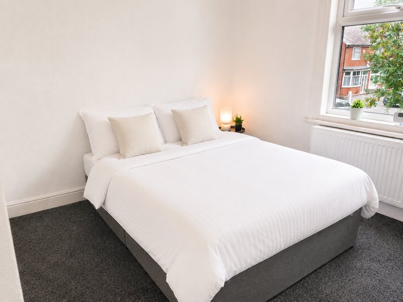 Bright bedroom with double bed, white bedding, cream pillows, dark carpet and window view