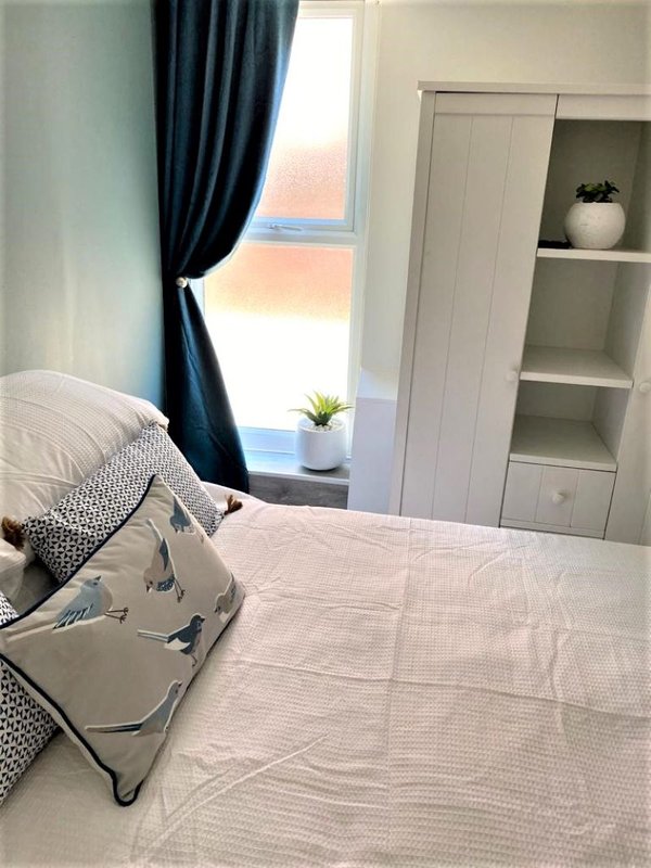 Bright bedroom with double bed, blue curtains, window with sea view, and white storage shelving
