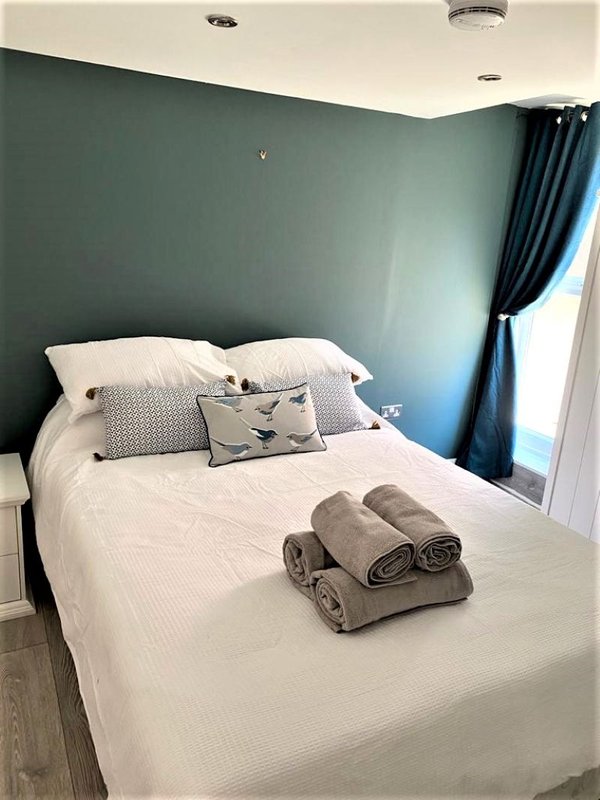 Bedroom with double bed, teal accent wall, white bedding, decorative pillows and rolled towels