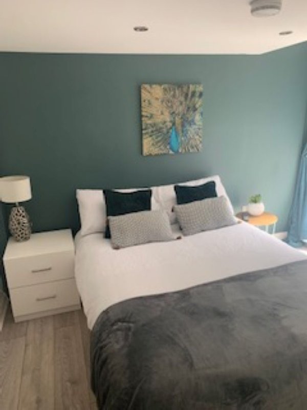 Bedroom with double bed, teal walls, white nightstands, and abstract wall art